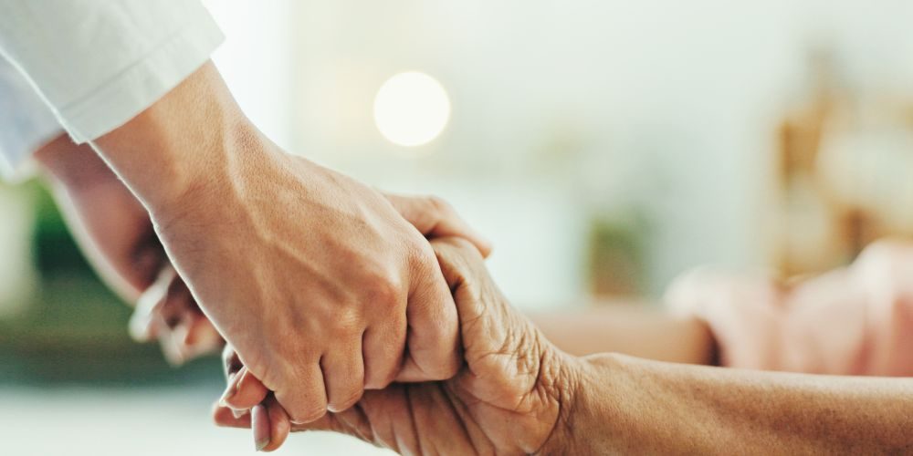 Händchen haltende Hände eines Pflegers und einer älteren Person, symbolisieren Fürsorge und Unterstützung