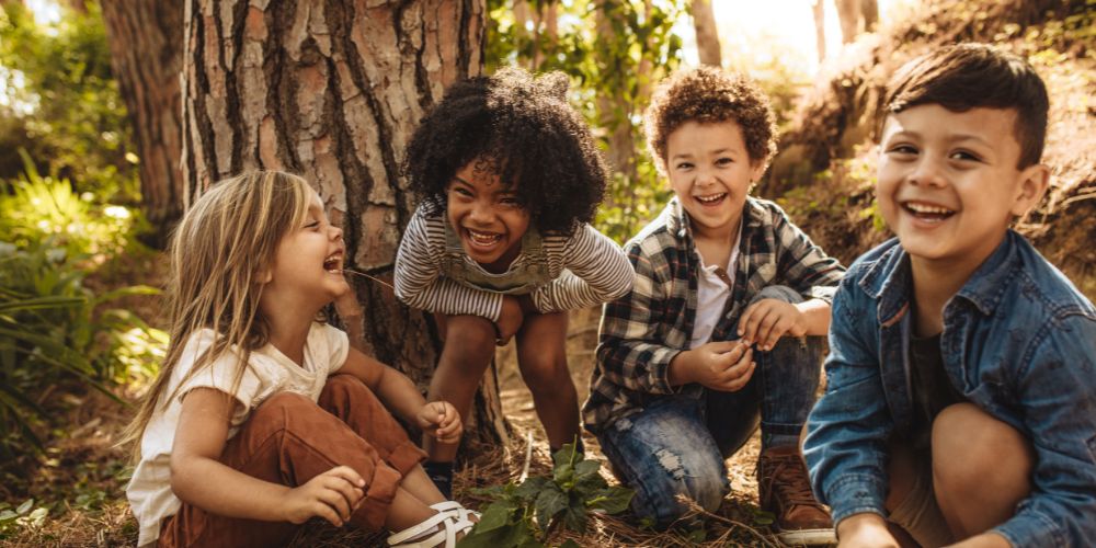 Gruppe von vier fröhlichen Kindern spielt und lacht im Wald, vermittelt Freude und Freundschaft