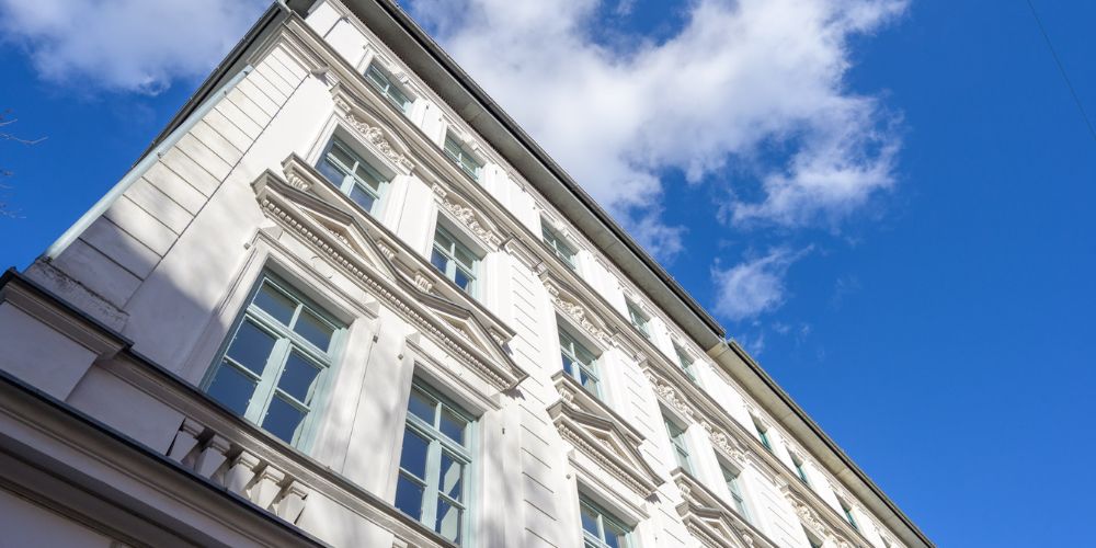 Elegante, denkmalgeschützte Altbau-Fassade eines Mehrfamilienhauses in München mit kunstvollen Stuckverzierungen, hohen Fenstern und blauem Himmel