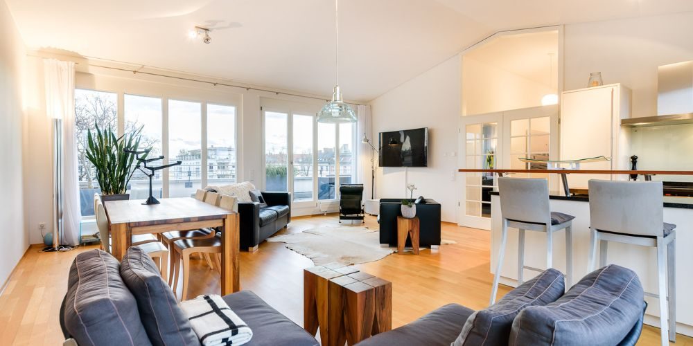 Großzügiger Wohn- und Essbereich mit Balkon in moderner Münchner Wohnung (30729) Heller, offener Wohn- und Essbereich einer Wohnung in München mit großer Fensterfront, Zugang zum Balkon, Parkettboden und moderner Einbauküche mit Barhockern