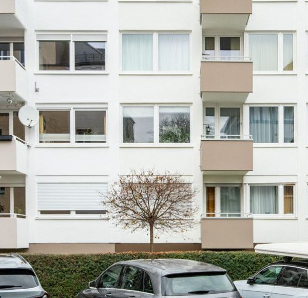 Frontansicht einer mehrgeschossigen Wohnanlage/Mehrfamilienhaus in München mit Balkonen, und parkenden Autos davor
