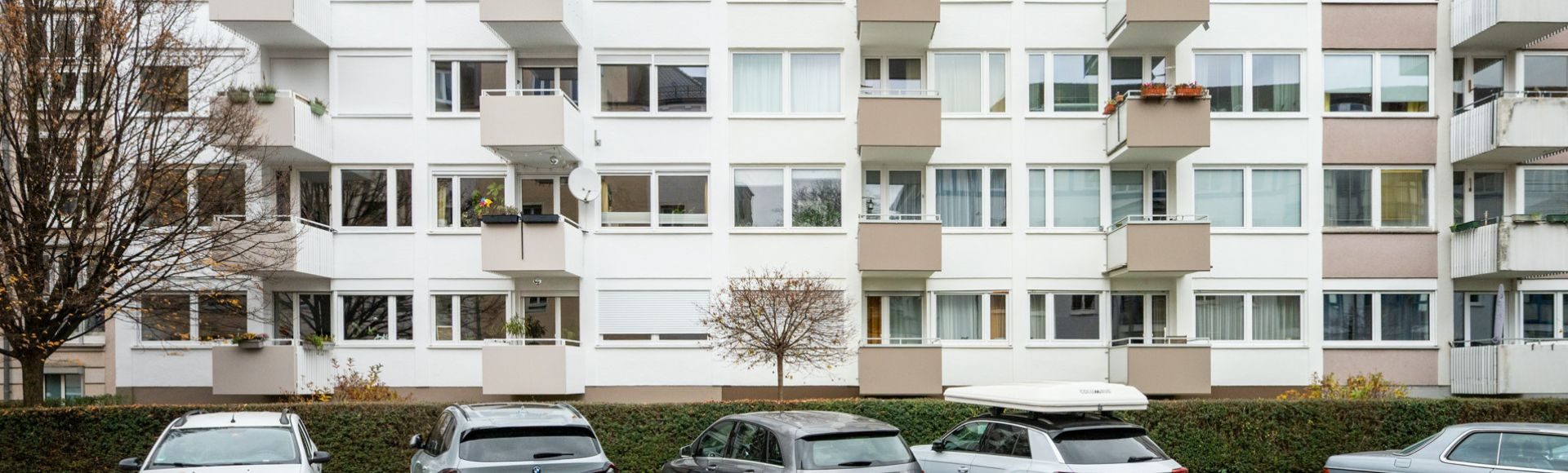 Frontansicht einer mehrgeschossigen Wohnanlage/Mehrfamilienhaus in München mit Balkonen, und parkenden Autos davor