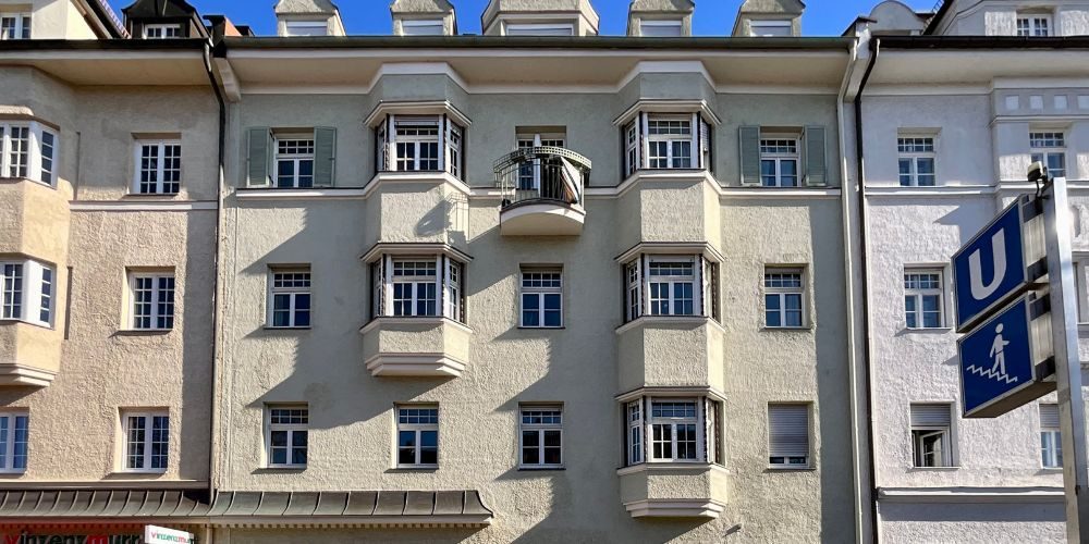 Fassadendetail eines Wohngebäudes mit mehreren Fenstern und Balkon, daneben ein U-Bahn-Schild
