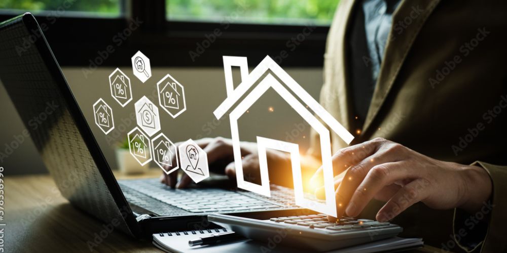 Person am Laptop mit grafischen Haus- und Finanzsymbolen