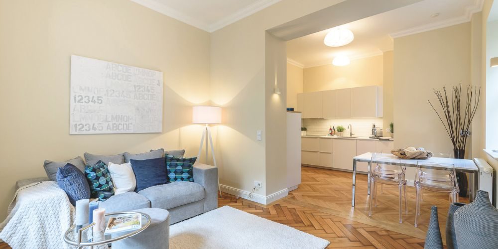 Helles und modern eingerichtetes Wohnzimmer mit Sofa, Couchtisch und offener Küche in einem stilvollen Raum mit Parkettboden