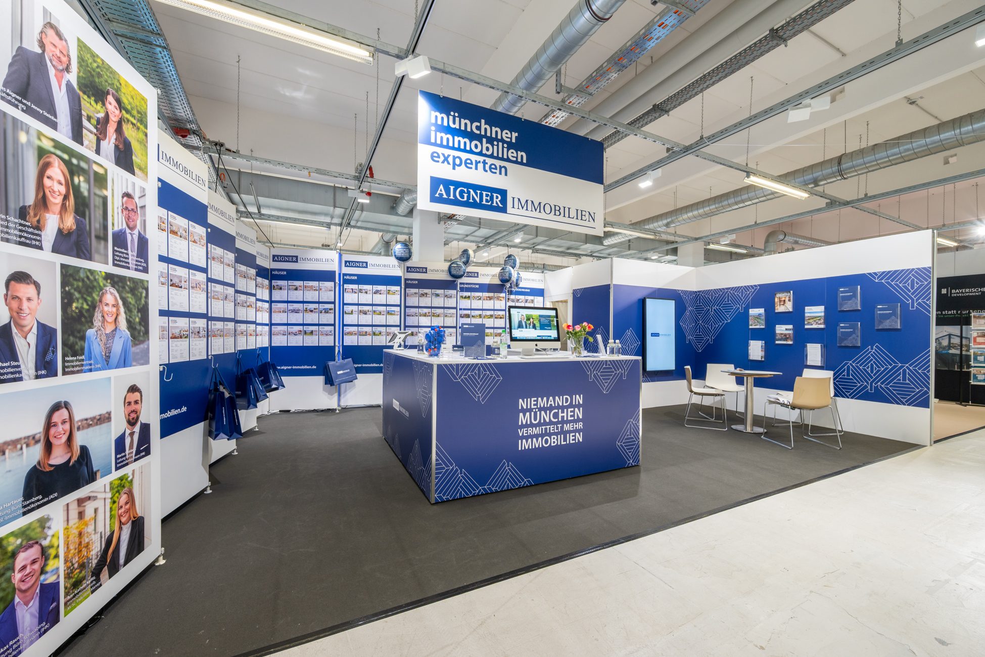 Moderner Messestand eines Immobilienmaklers in München: Aigner Immobilien präsentiert aktuelle Angebote, Dienstleistungen und Expertenwissen rund um Kauf, Verkauf und Bewertung von Immobilien.