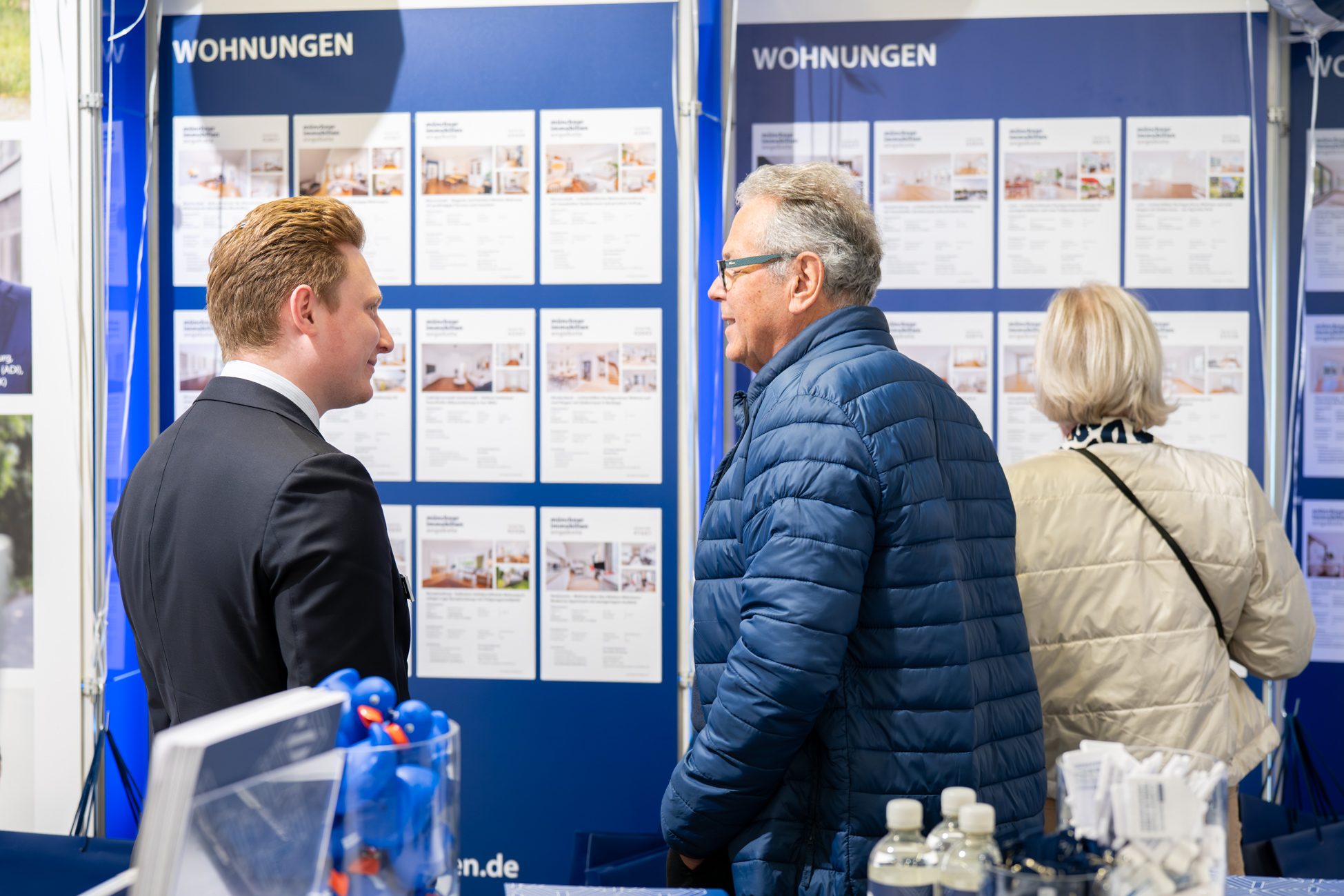 Besucher einer Immobilienmesse in München prüfen aktuelle Wohnungsangebote und Exposés. Direkter Austausch mit Maklern und Einblicke in den Münchner Immobilienmarkt.