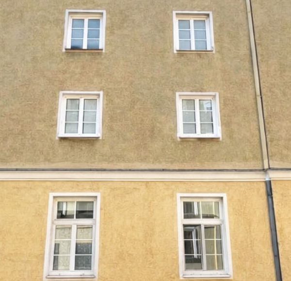 Fassadensicht eines gelben Mehrfamilienhauses mit mehreren Fenstern und einem modernen Eingangsbereich