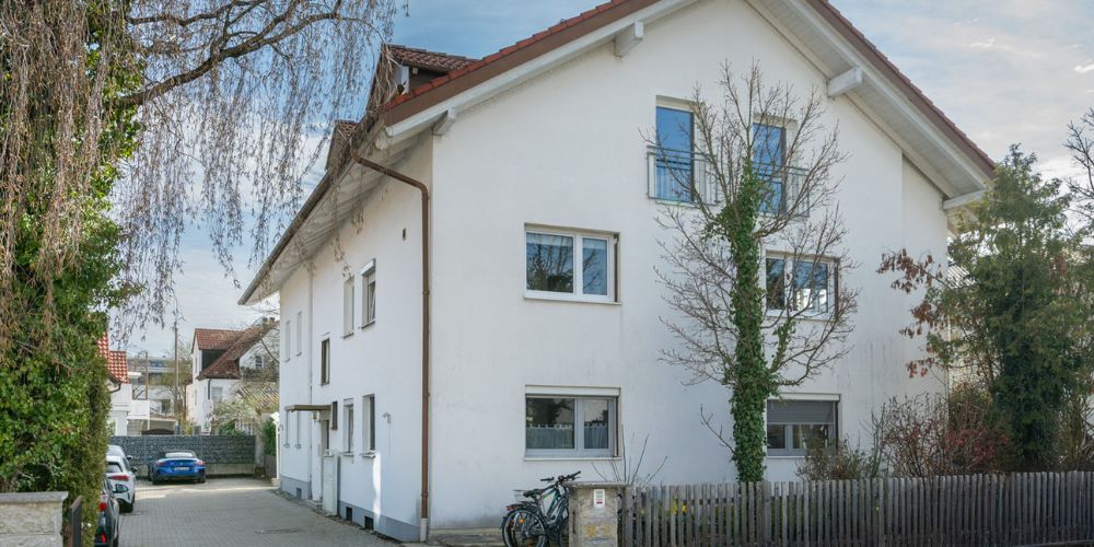 Ansicht eines Mehrfamilienhaues mit Spitzdach und kleinem Garten davor
