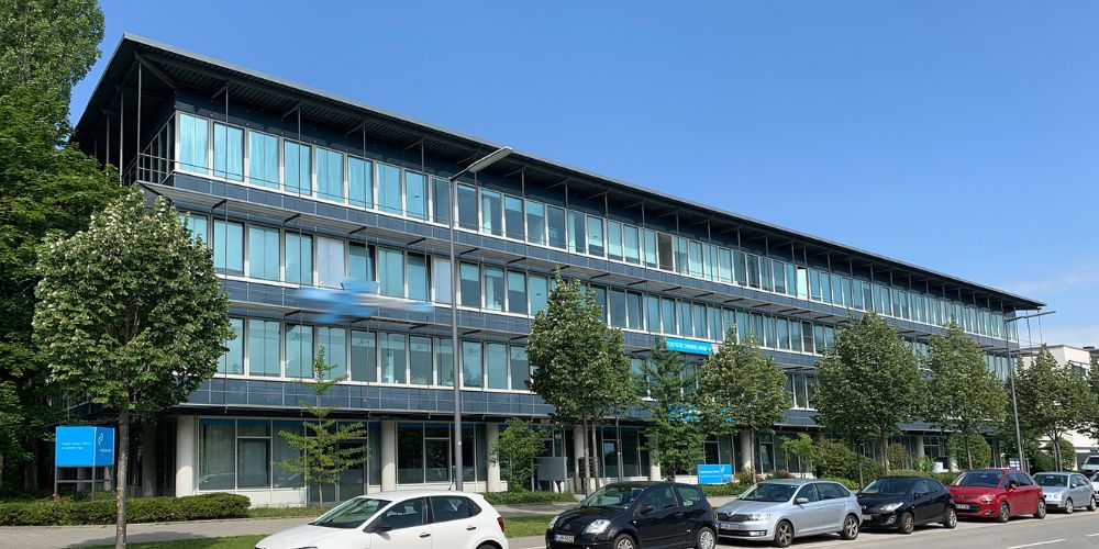 Modernes Bürogebäude in München mit Glasfassade, Bäumen und Parkplätzen vor dem Eingang