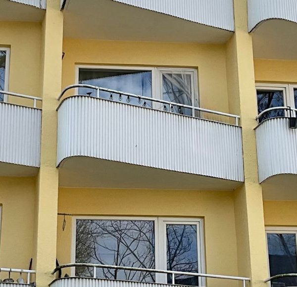 Außenansicht eines Mehrfamilienhauses mit mehreren Balkonen, gelber Fassade und großen Fenstern in München