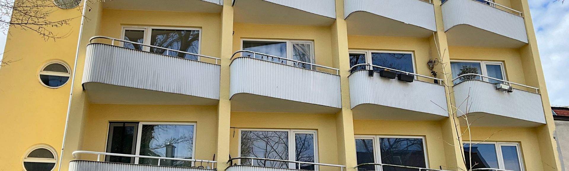 Außenansicht eines Mehrfamilienhauses mit mehreren Balkonen, gelber Fassade und großen Fenstern in München