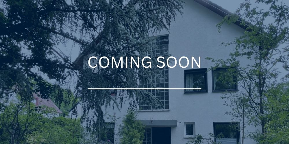 Helles Mehrfamilienhaus mit Bäumen davor