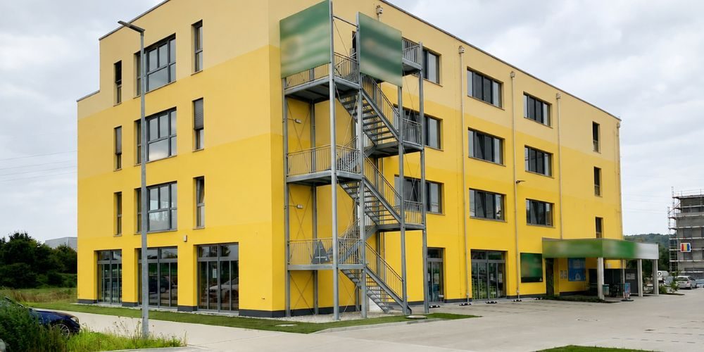 Außenansicht eines gelben Gewerbegebäudes (36429) Außenansicht eines gelben Gewerbegebäudes mit Metalltreppe, großen Fenstern und Eingangsbereich