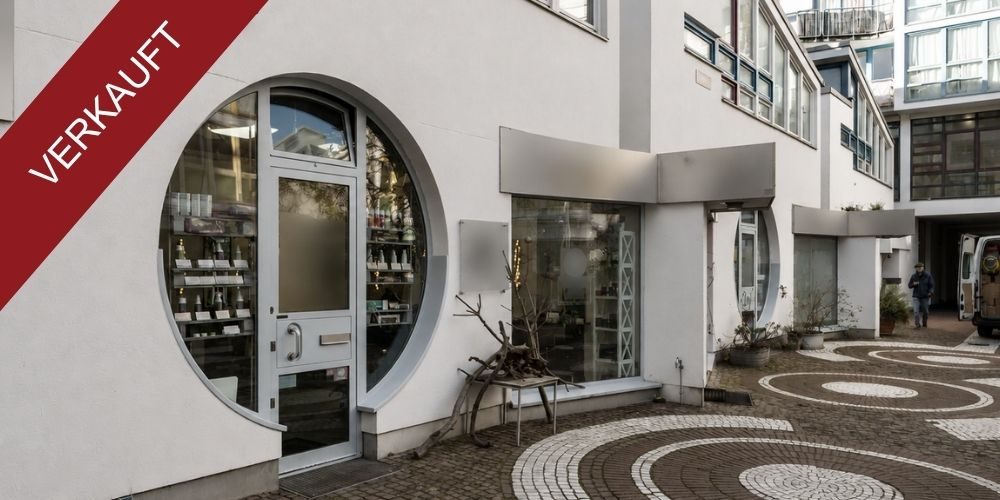 Außenansicht eines verkauften Ladenlokals mit rundem Schaufenster, Eingangstür und Innenhofbereich