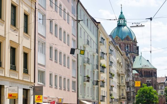 Mehrfamilienhäuser entlang einer Straße in München mit Blick auf die Kuppel St. Lukas Kirche