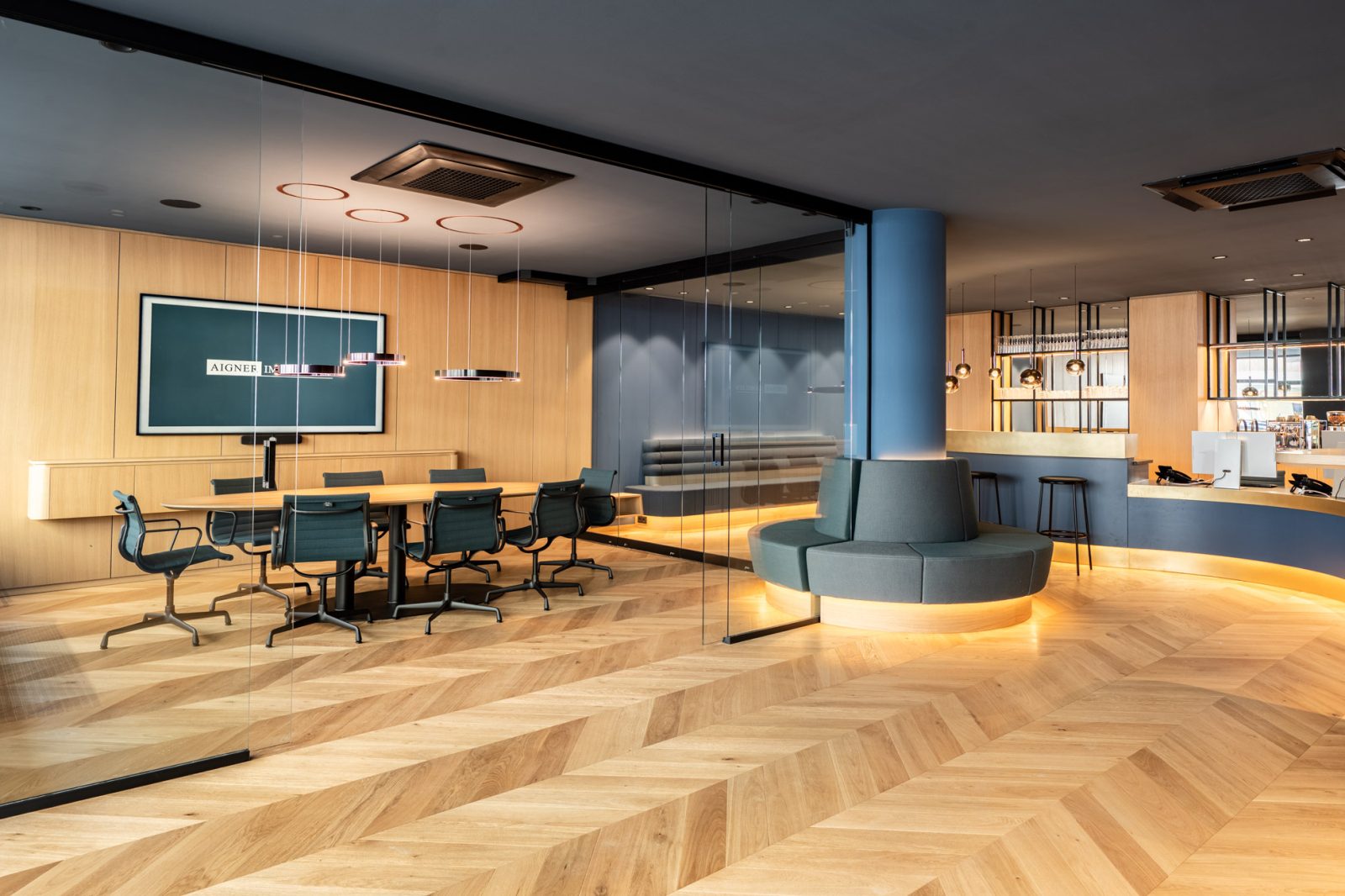 Moderner Besprechungsraum mit Glaswänden, Designleuchten, Fischgrätparkett und offenem Empfangsbereich im Büro von Aigner Immobilien in München