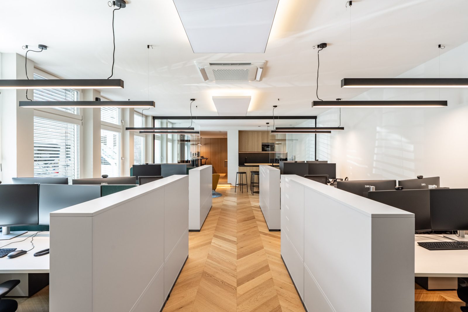 Heller Open-Space-Bereich mit ergonomischen Arbeitsplätzen, Glasabtrennung, Fischgrätparkett und moderner Beleuchtung im Immobilienbüro in München