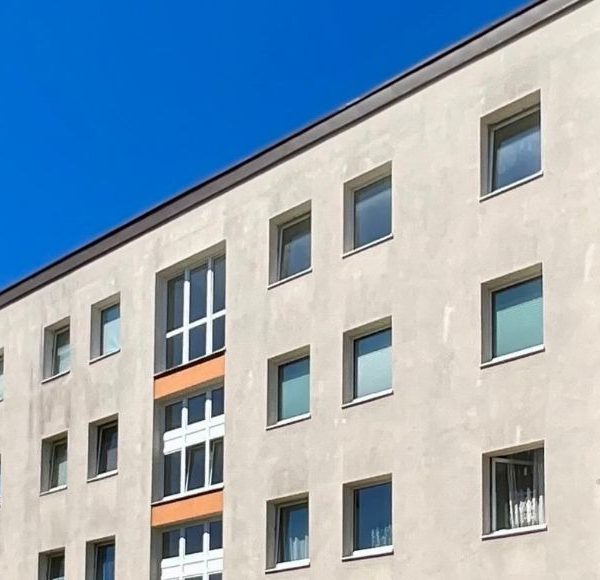 Außenansicht eines mehrgeschossigen Mehrfamilienhauses in München mit heller Fassade und großen Bäumen