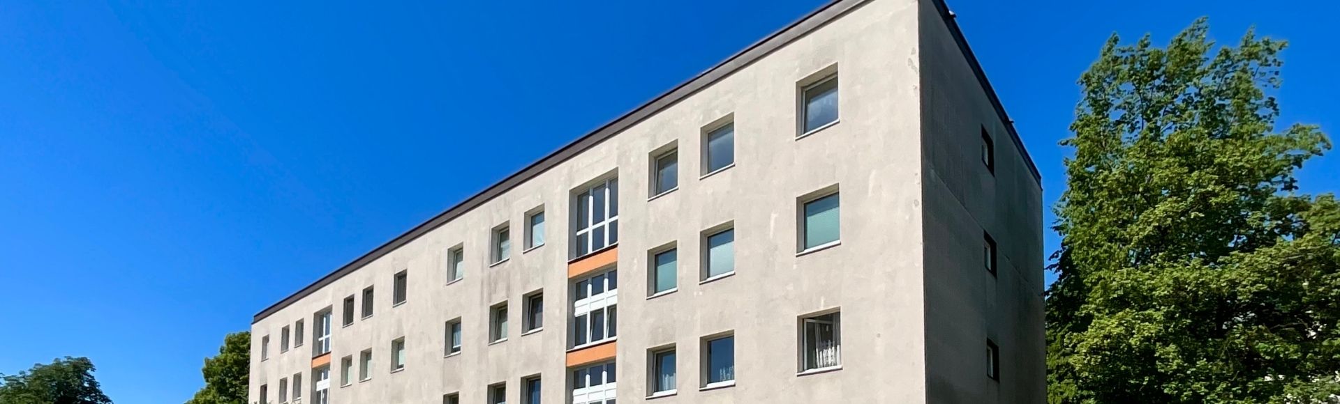 Außenansicht eines mehrgeschossigen Mehrfamilienhauses in München mit heller Fassade und großen Bäumen