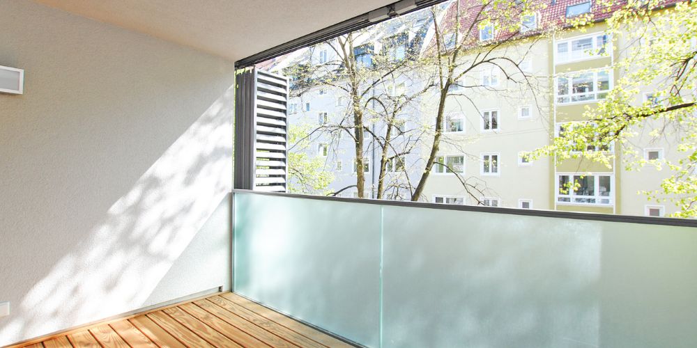 Heller Balkon mit Glasbrüstung und Blick auf begrünte Innenhoflage in München