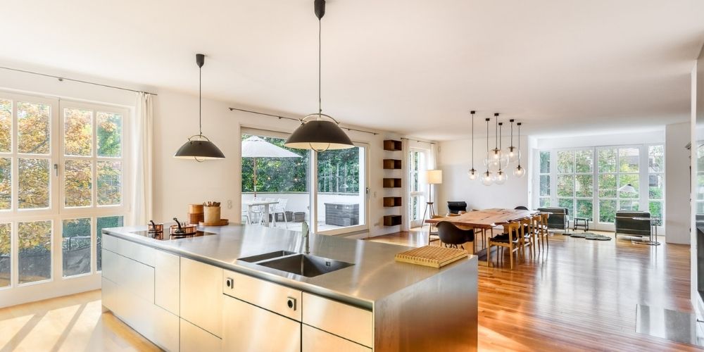 Helle offene Wohnküche mit großer Kochinsel, Essbereich, Holzboden und Zugang zur Terrasse in moderner Münchner Immobilie