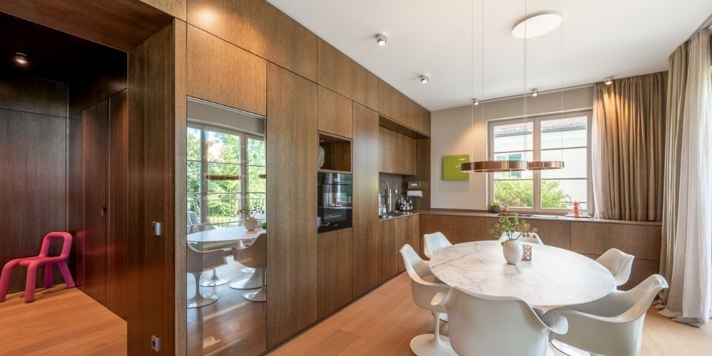 legante Wohnküche mit maßgefertigter Holzfront, integriertem Essbereich, rundem Esstisch und moderner Ausstattung in hochwertiger Wohnung in München