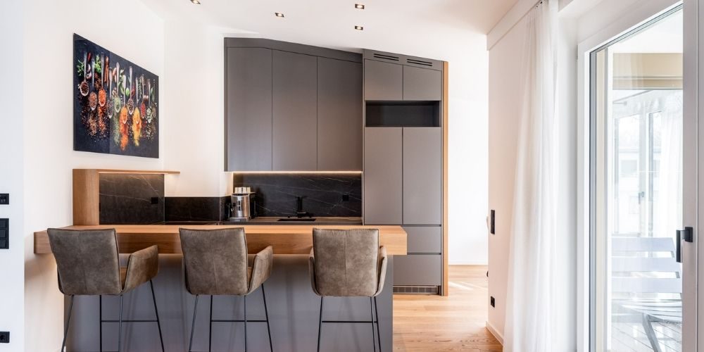Moderne Einbauküche mit Kücheninsel, dunklen Fronten, Holzarbeitsplatte und stilvollem Essbereich in hochwertiger Münchner Wohnung