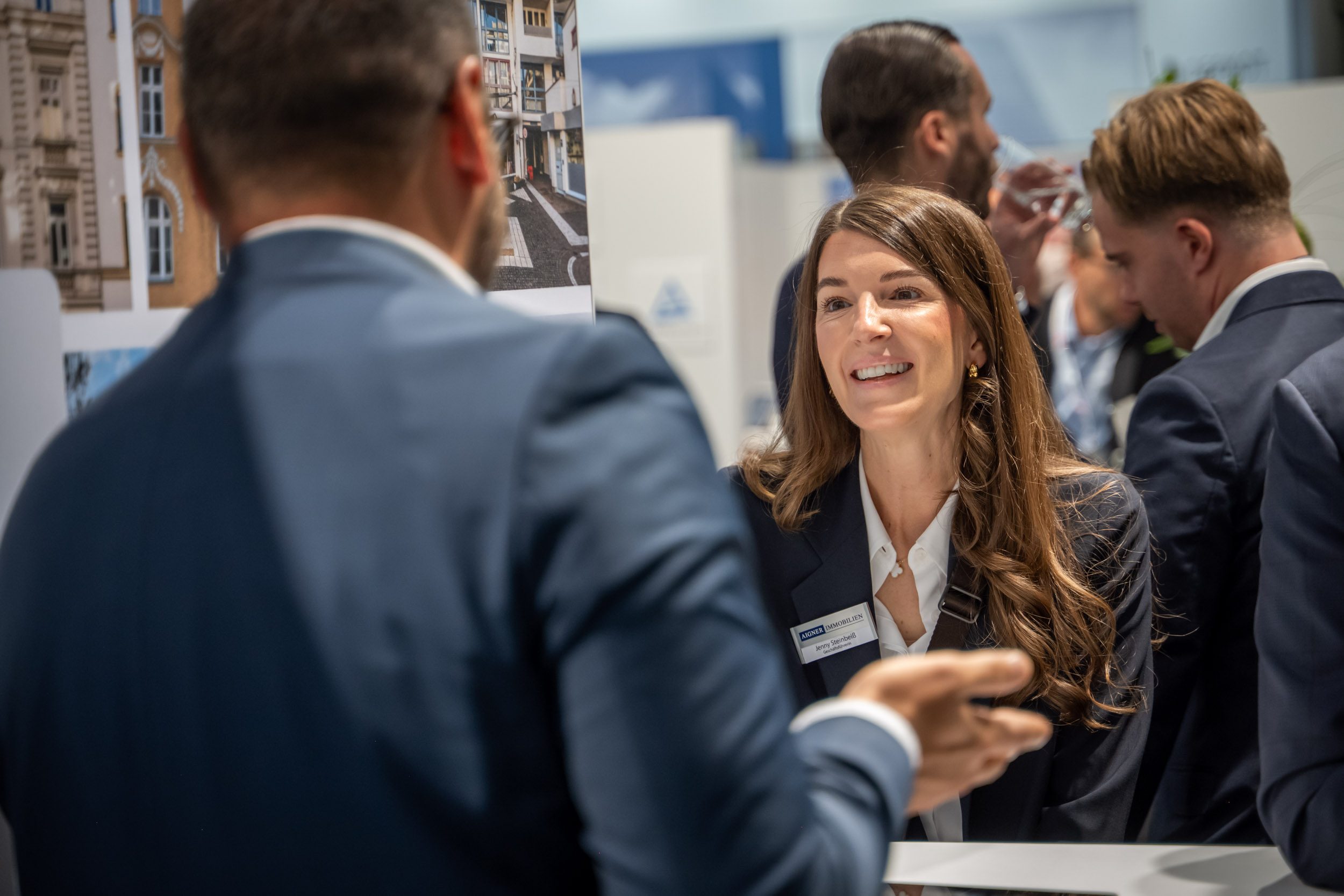 Geschäftsführerin im Gespräch am Messestand Geschäftsführerin von Aigner Immobilien lacht im Gespräch mit einem Messebesucher vor Gebäudefotos