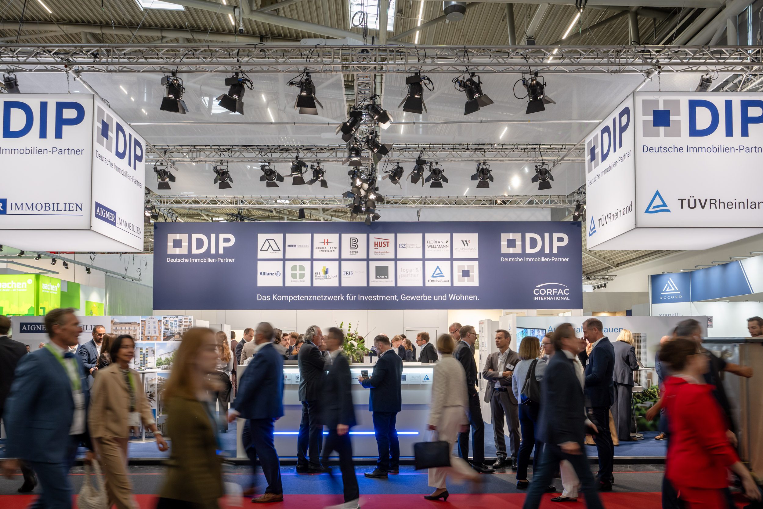DIP-Gemeinschaftsstand auf der Immobilienmesse DIP-Messestand mit Partnerlogos und Slogan „Kompetenznetzwerk für Investment, Gewerbe und Wohnen“, davor eilende Besucher