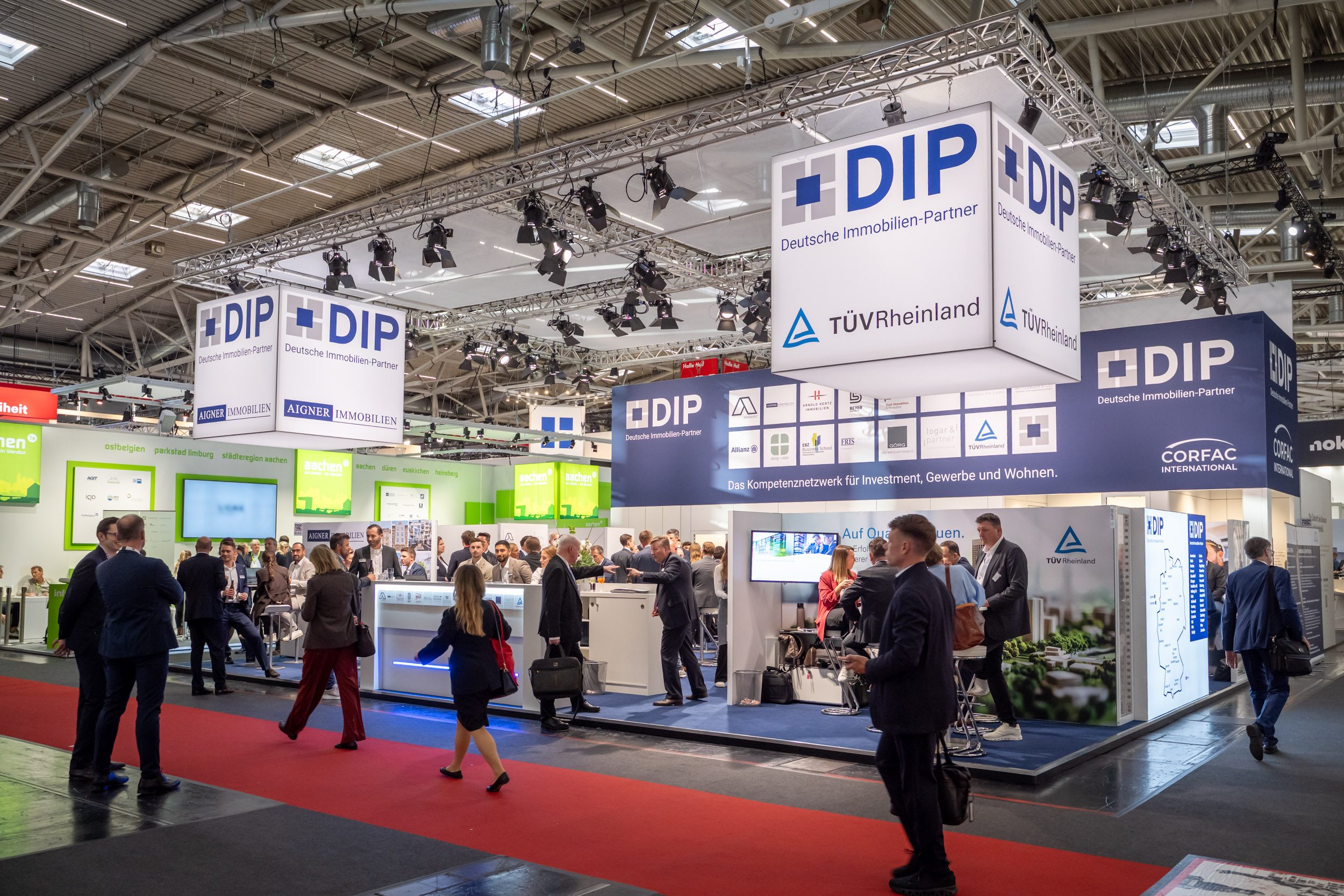 Messehalle mit DIP-Stand und Aigner-Branding Messehalle mit großem DIP-Gemeinschaftsstand, hängenden Leuchtwürfeln mit Aigner-Immobilien-Logo und rotem Teppich