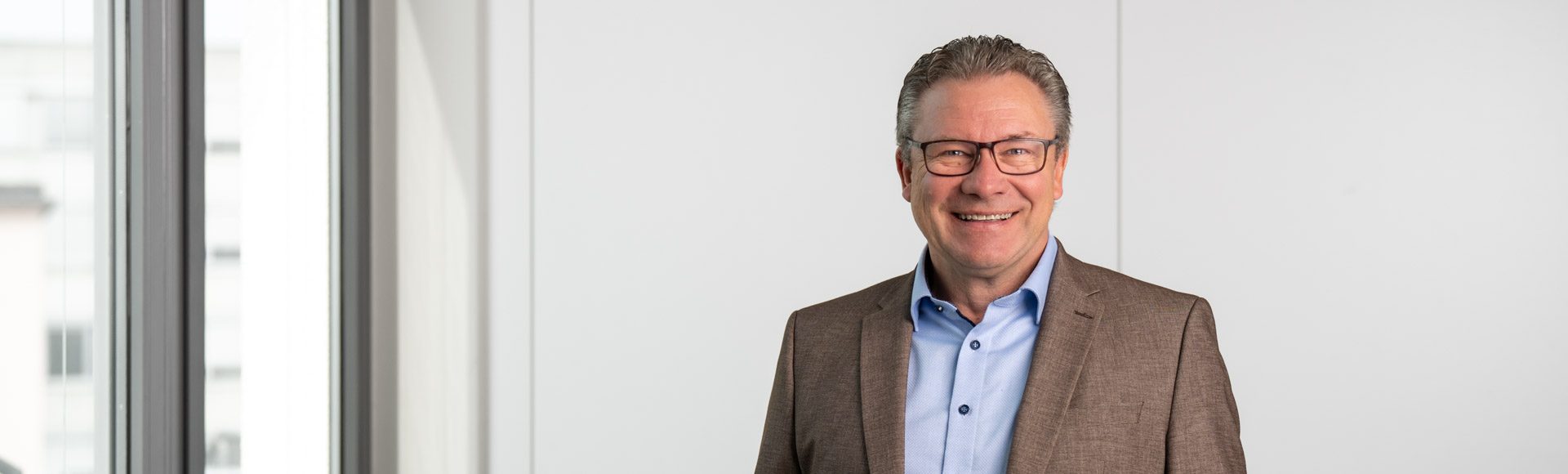 Finanzierungsberater im grau-braunen Anzug vor weißer Wand