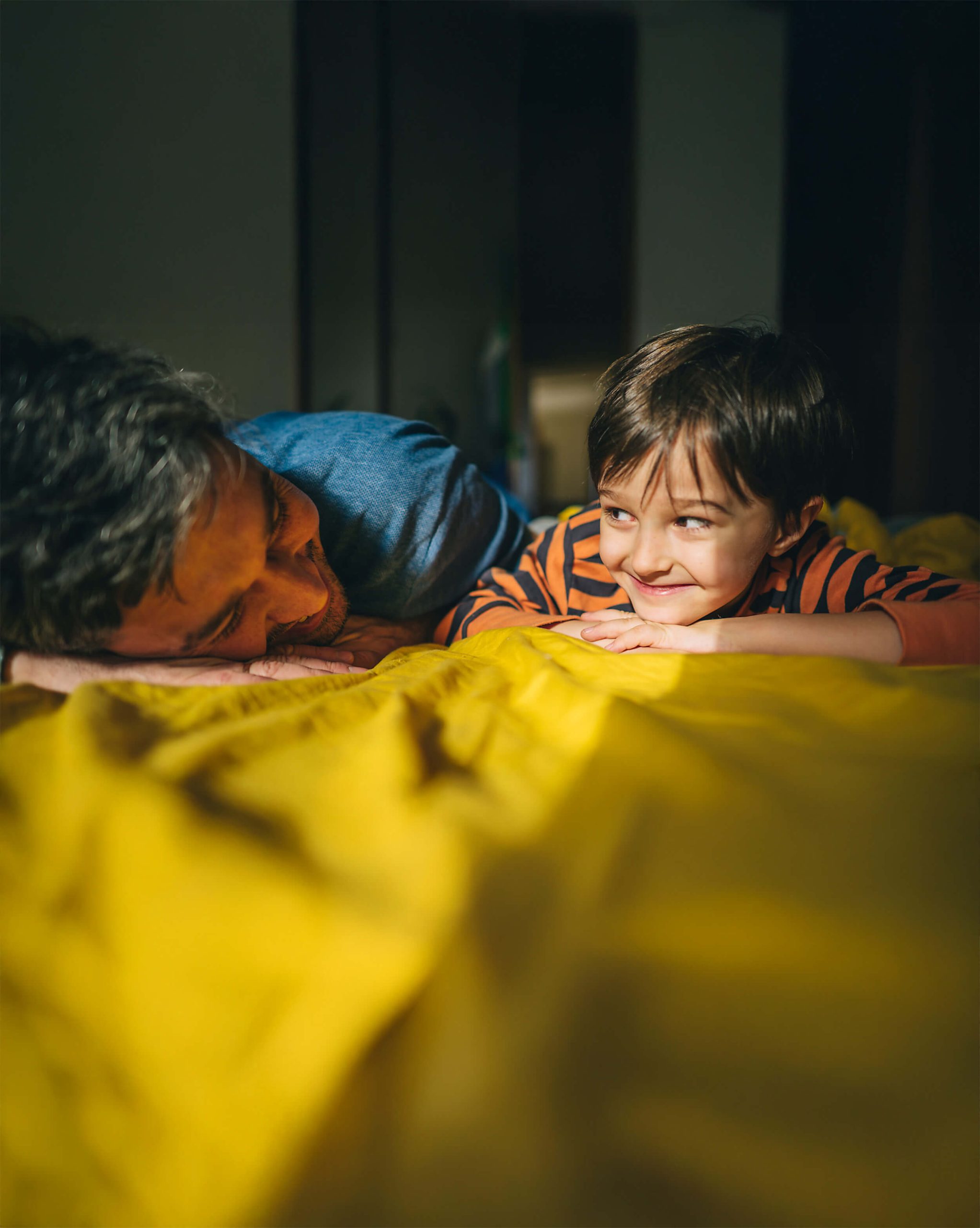 Vater und Sohn liegen entspannt auf einem Bett und laecheln sich liebevoll an