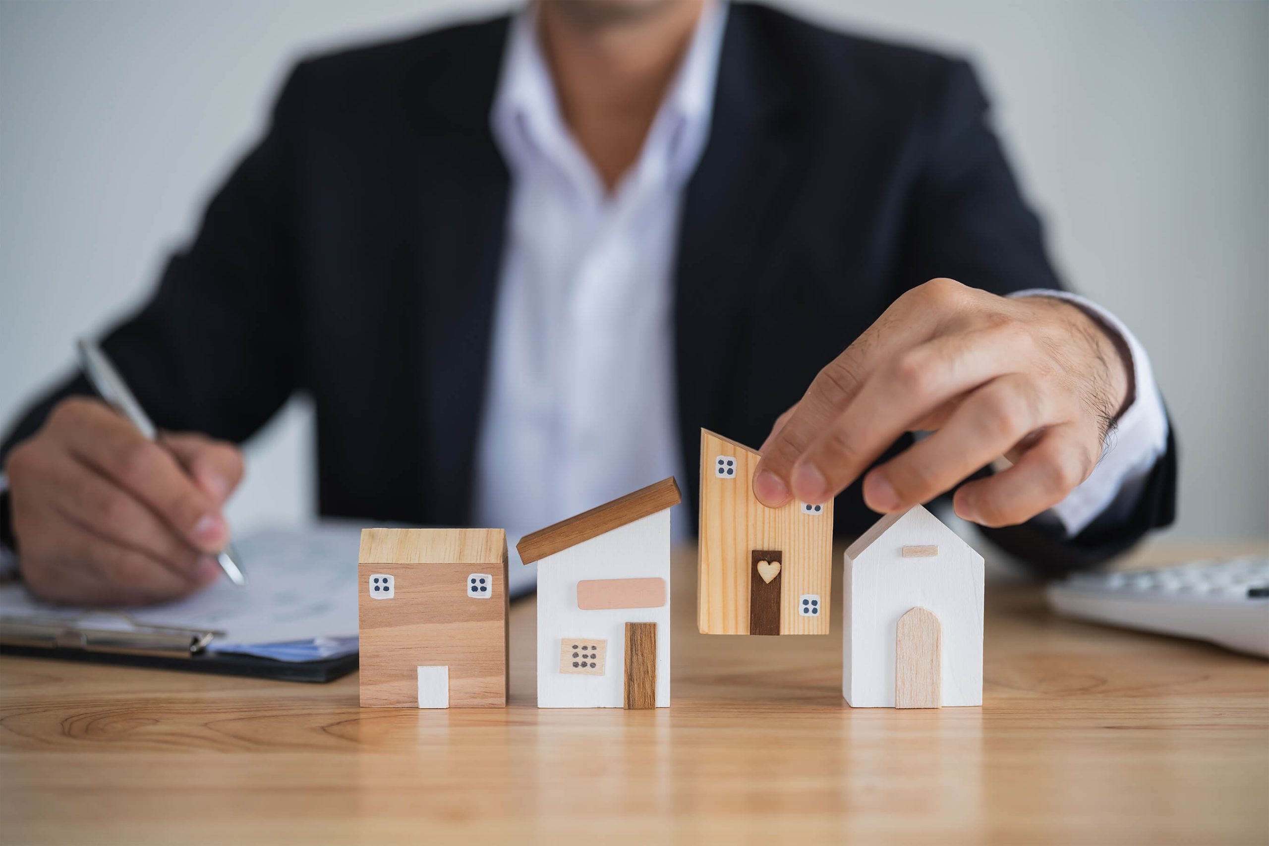 Immobilienmakler hält symbolisch ein Holzmodellhaus für Immobilien und deren Bewertung Immobilienmakler hält symbolisch ein Holzmodellhaus für Immobilien und deren Bewertung