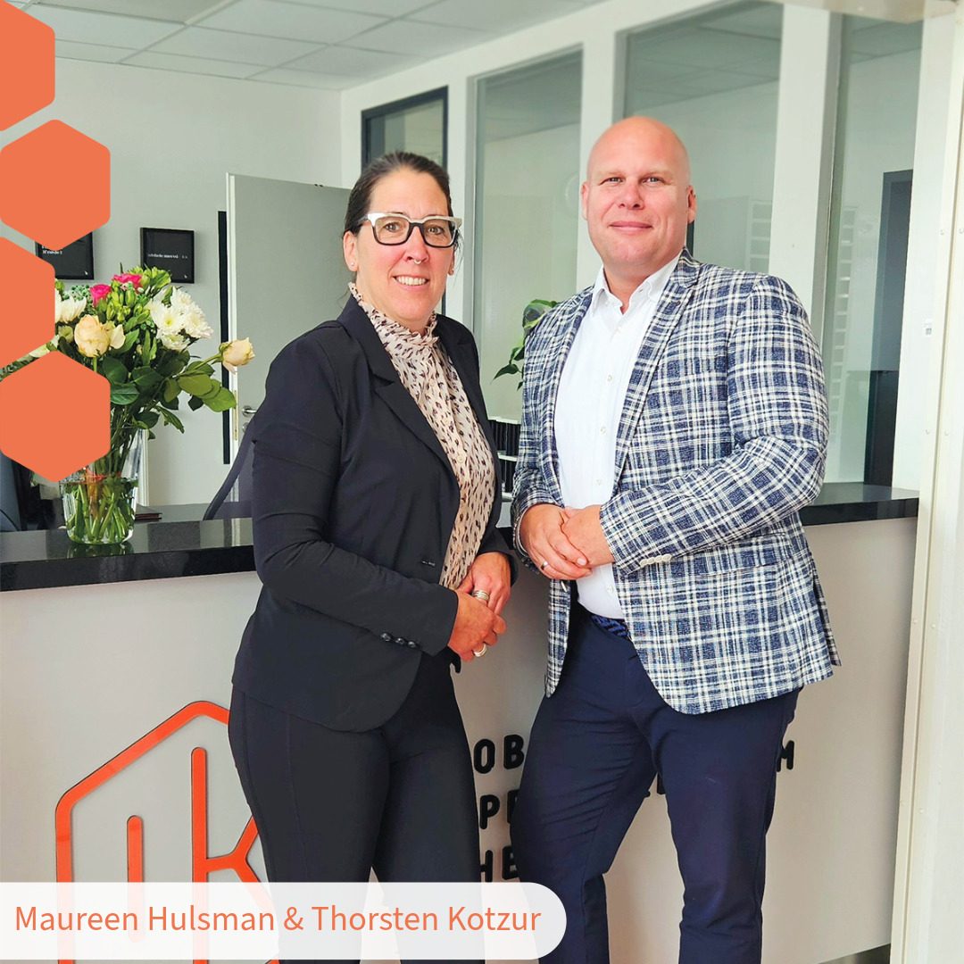 Thorsten Kotzur von Kotzur Immobilien Aachen und Maureen Hulsman von GRENSimmo Vaals stehen lächelnd nebeneinander und präsentieren ihre neue Immobilien-Kooperation für das Dreiländereck. Professionelles Teambild der beiden inhabergeführten Immobilienmakler für Aachen und die Niederlande.