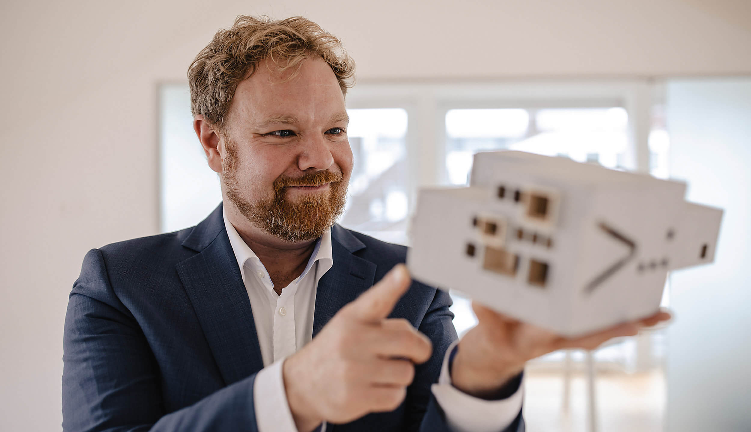 Mann im Anzug hält ein Architekturmodell hoch und zeigt darauf - Wüstenrot Immobilien