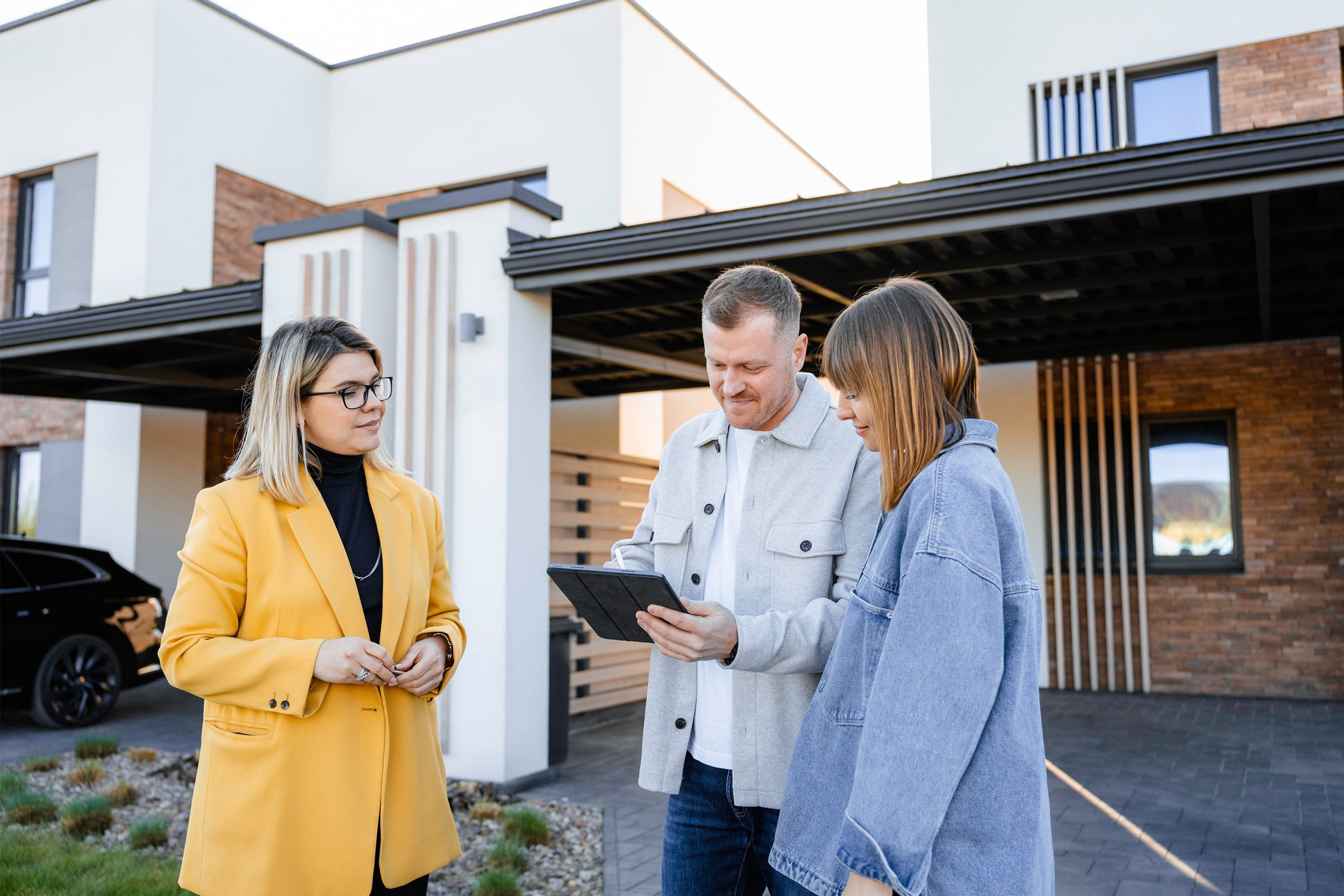 Hausverkaufsgespraech mit Maklerin vor moderner Immobilie