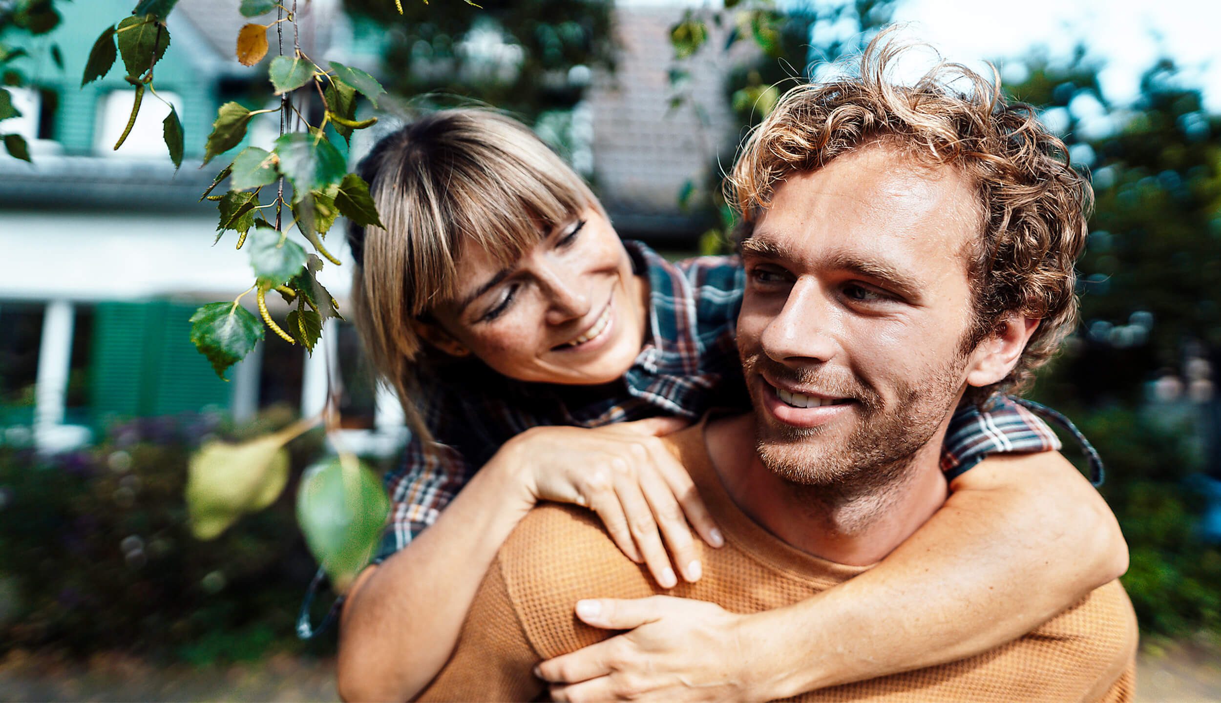 Junges Paar vor ihrem neuen Zuhause, lachend und gluecklich im Garten