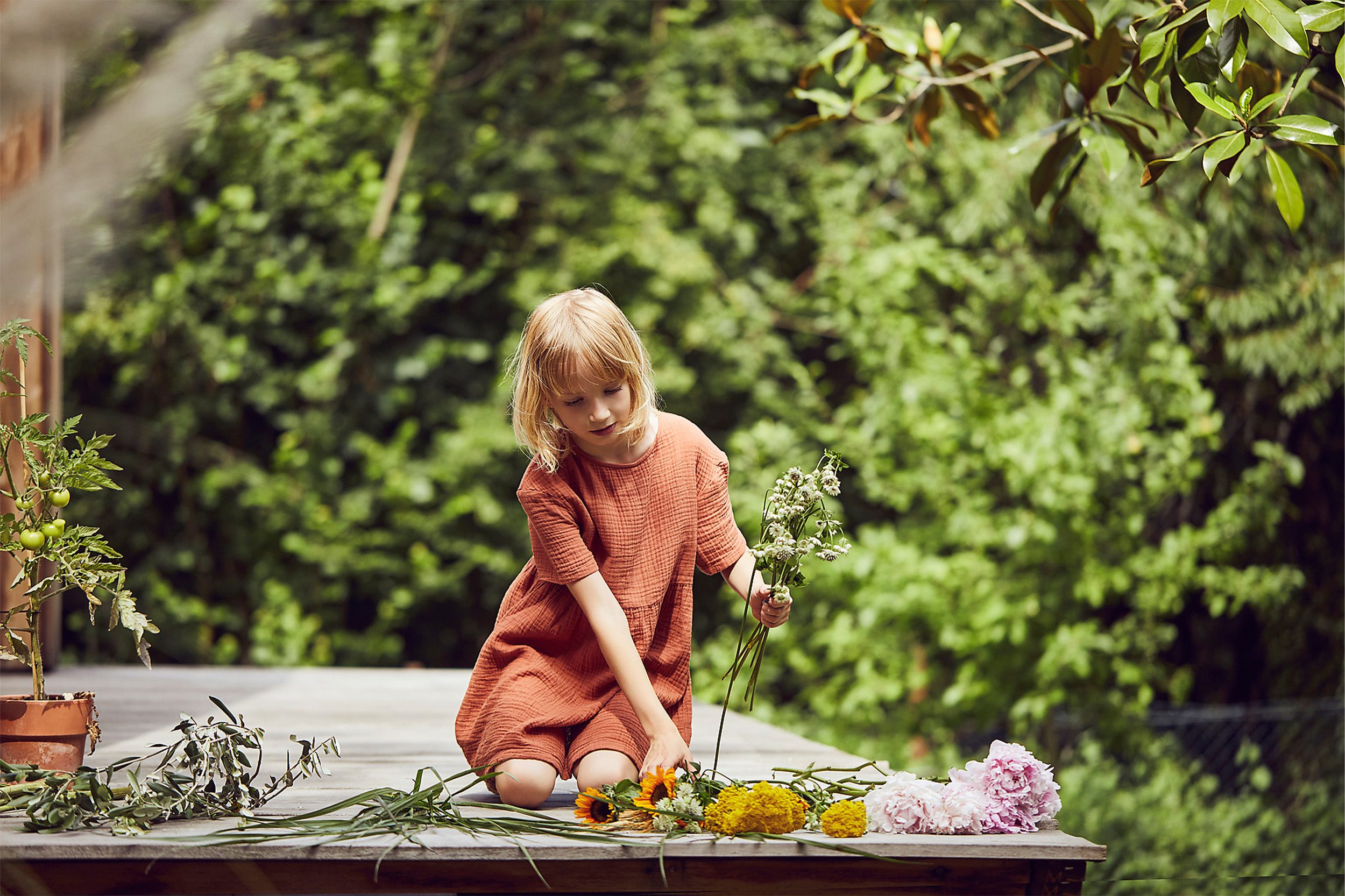 Kind sitzt auf einer Holzterrasse und sortiert bunte Blumen Kind sitzt auf einer Holzterrasse und sortiert bunte Blumen - Wüstenrot Immobilien