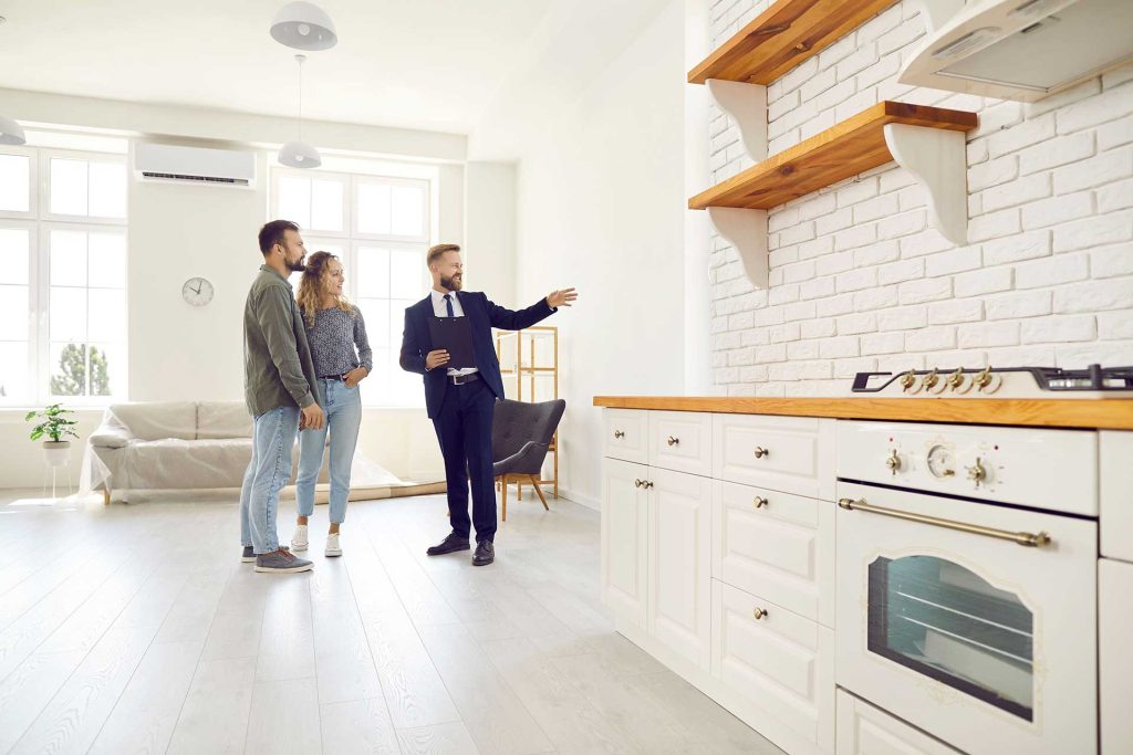 Immobilienmakler führt junges Paar durch eine Küche im Haus