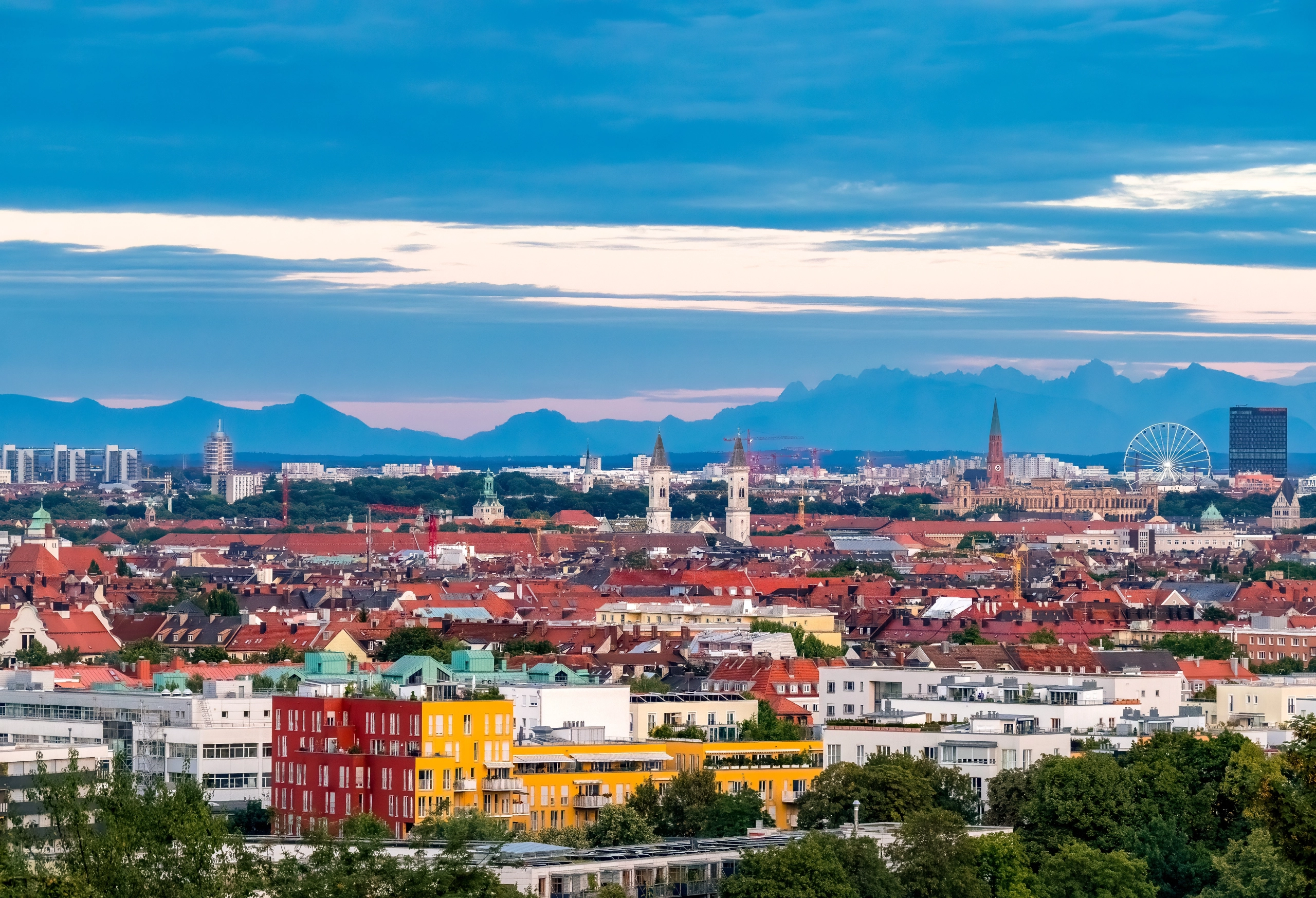 Stadtpanorama mit Blick auf Münchens Wohngebiete und die Alpen im Hintergrund. Symbolbild für steigende Preise im Wohnbestand durch Standortqualität, Infrastruktur und begrenzte Neubauten.