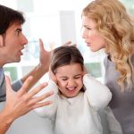 Ein streitendes Elternpaar steht sich wütend gegenüber, während ihre Tochter sich mit schmerzverzerrtem Gesicht die Ohren zuhält – ein eindrückliches Symbol für familiäre Konflikte, die Kinder emotional belasten.